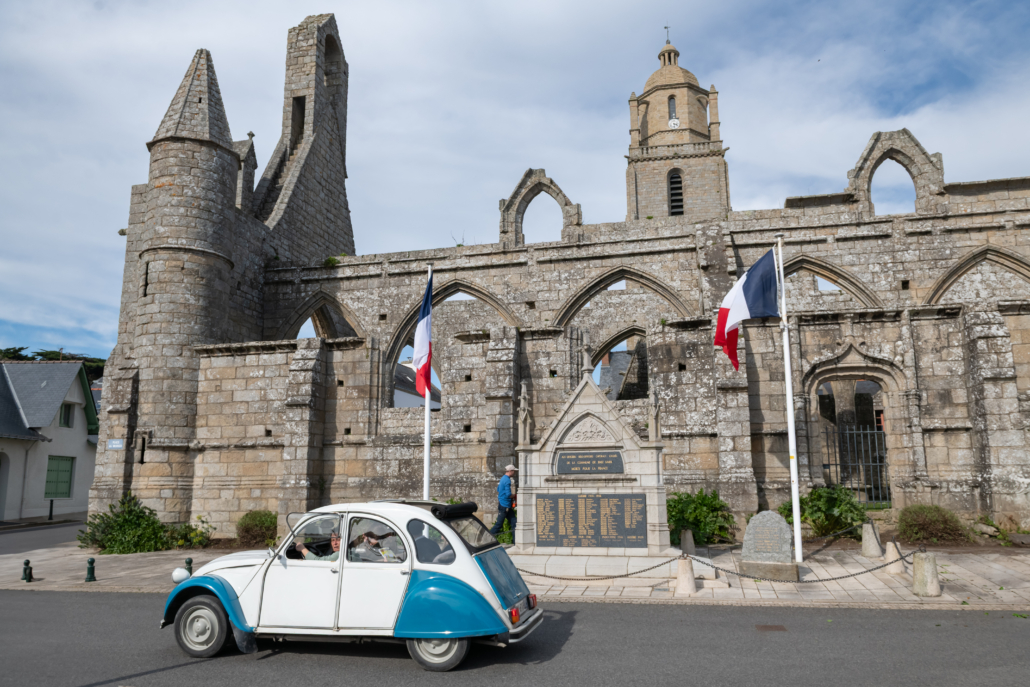 Citroën 2CV circulant devant un monument historique dans le cadre d'un rallye culturel et touristique.