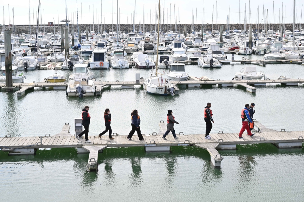 Équipes marchant sur les pontons d’un port de plaisance pour rejoindre les voiliers de la régate.