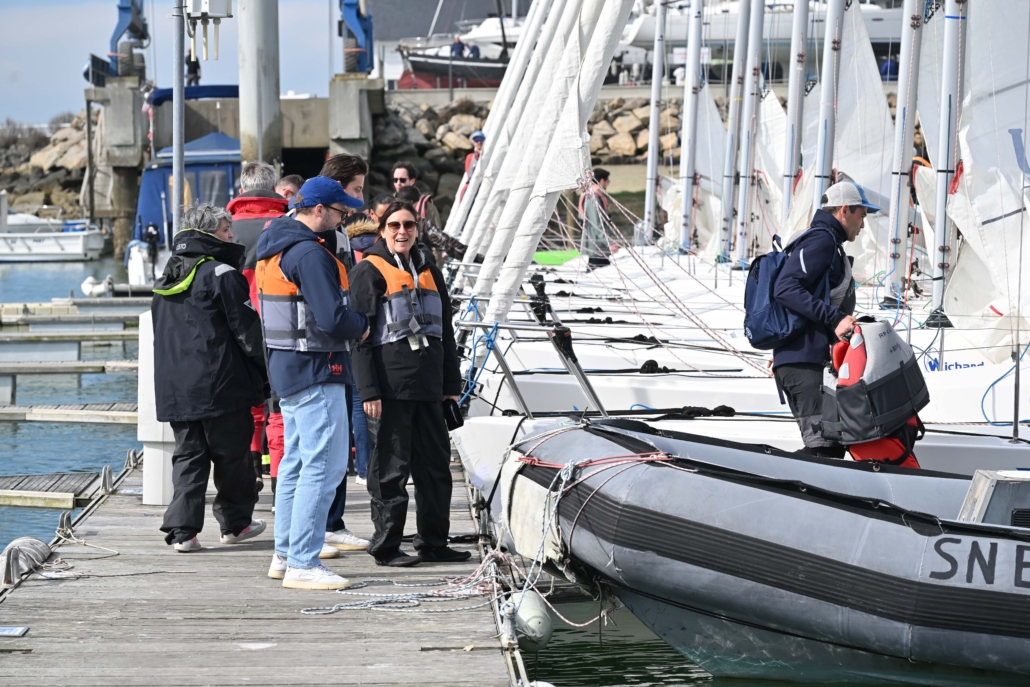 Participants et skippers préparant les voiliers avant le départ d’un challenge nautique en équipe.