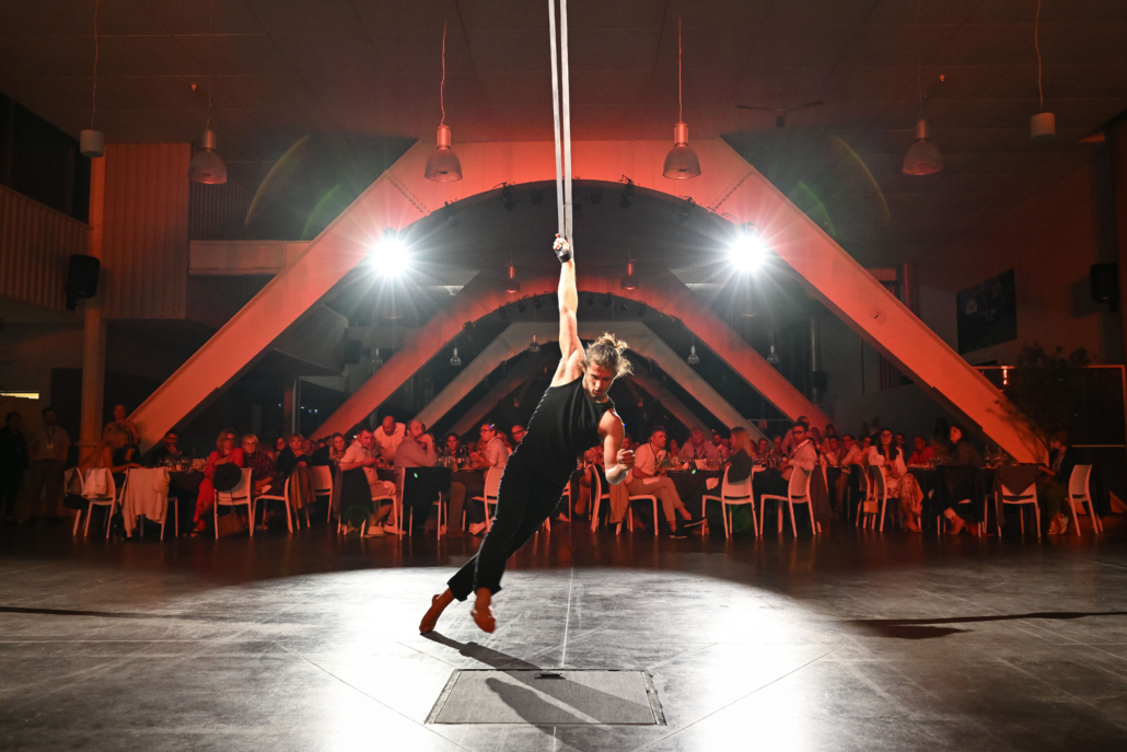 Un artiste réalise une performance aérienne au centre de la salle devant les participants réunis pour une soirée événementielle.