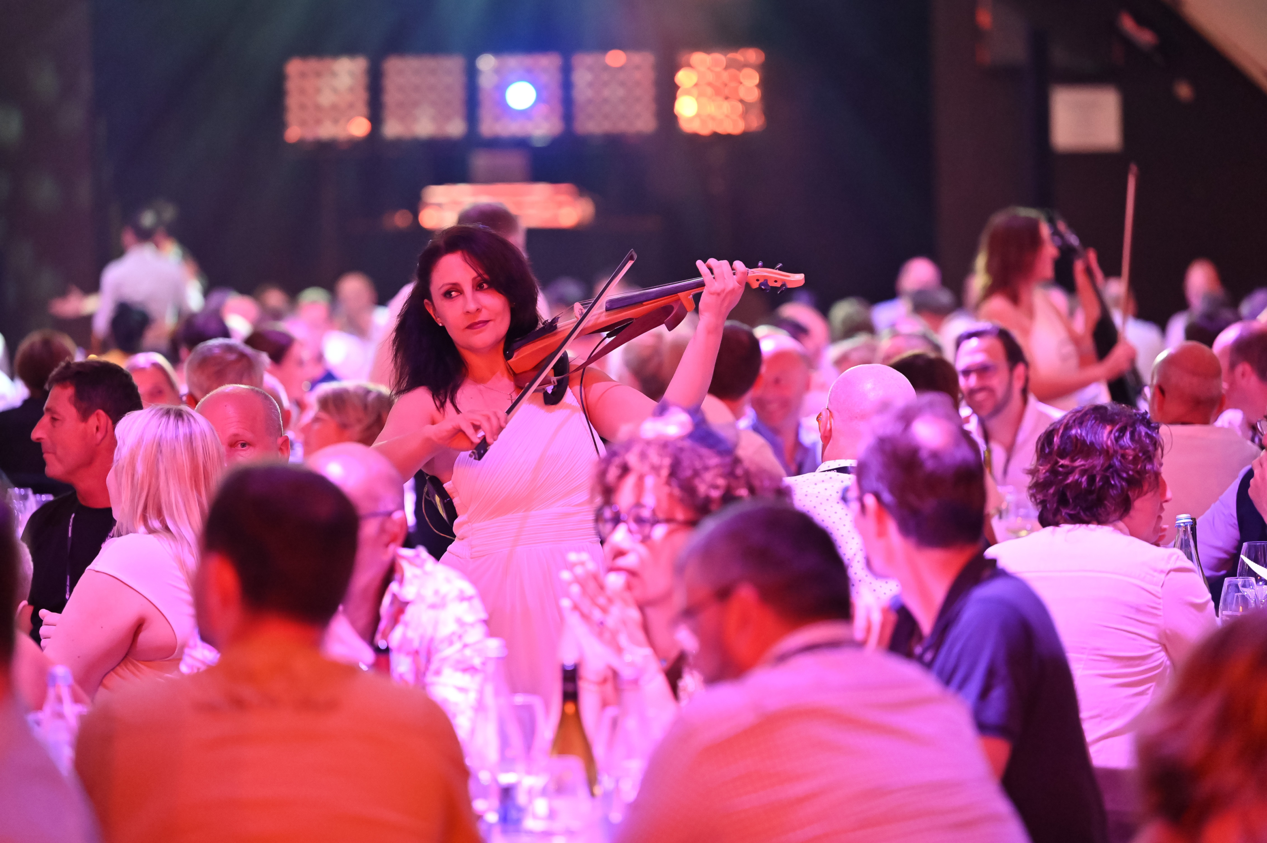 Une musicienne joue du violon électrique au milieu des convives lors d'un dîner de gala.