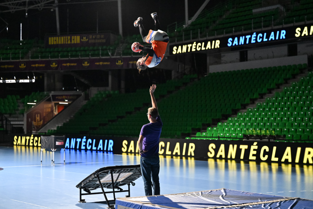 Athlète effectuant un salto avec ballon devant les spectateurs d’un événement d’entreprise.