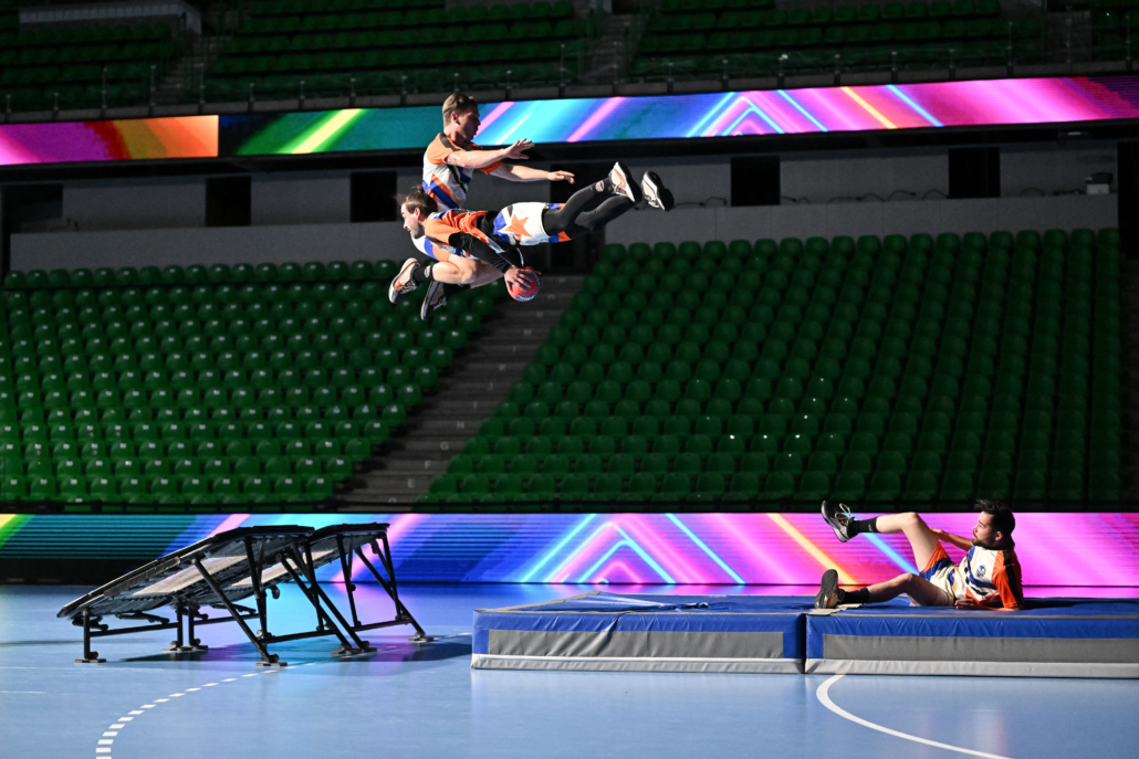 Deux athlètes en plein saut synchronisé lors d’un spectacle sportif indoor.