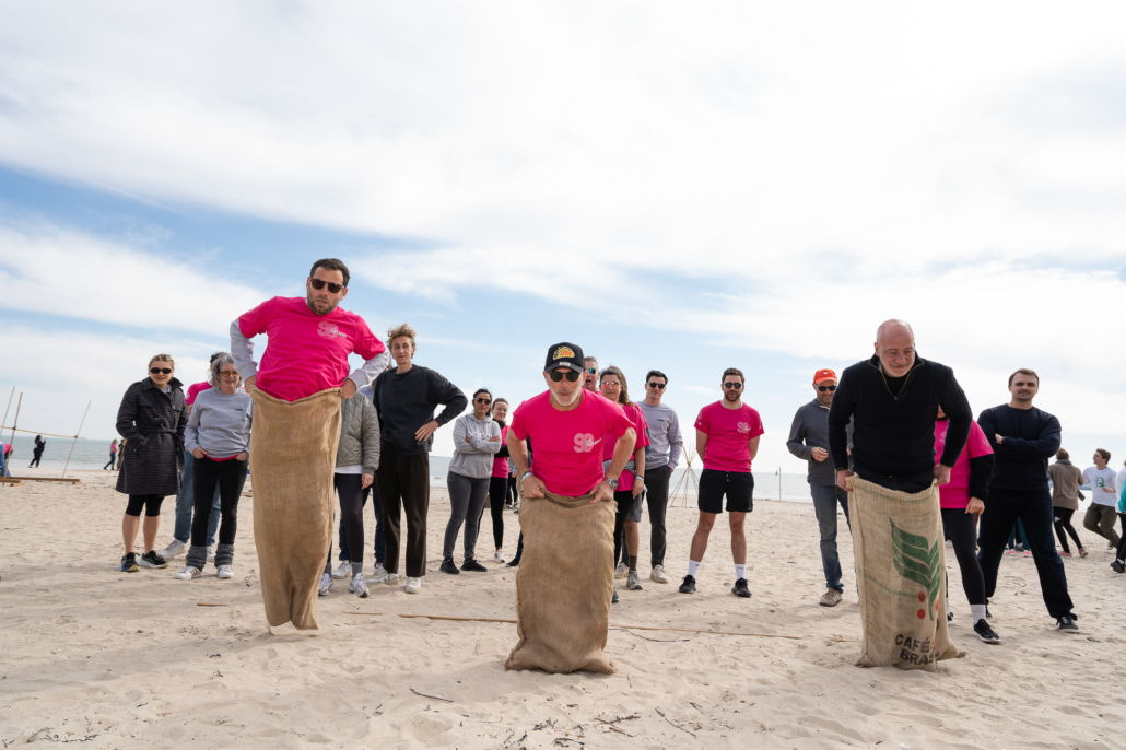 Participants s’affrontant lors d’une course en sacs sur la plage dans le cadre d’un challenge de cohésion d’entreprise.