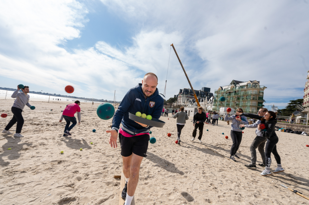 Participant transportant des balles en équilibre pendant une activité de cohésion sur la plage.