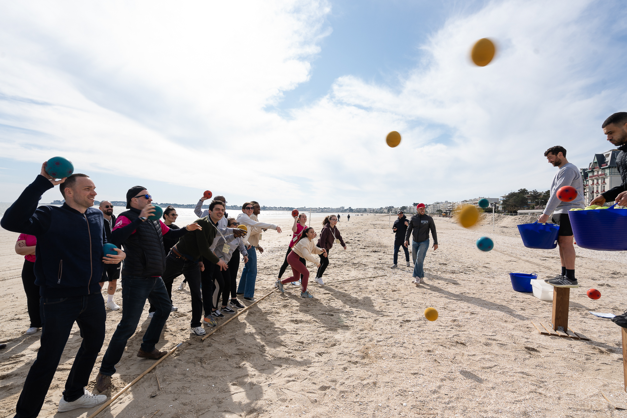 Groupe de collaborateurs participant à un défi collectif de lancer de balles sur la plage.