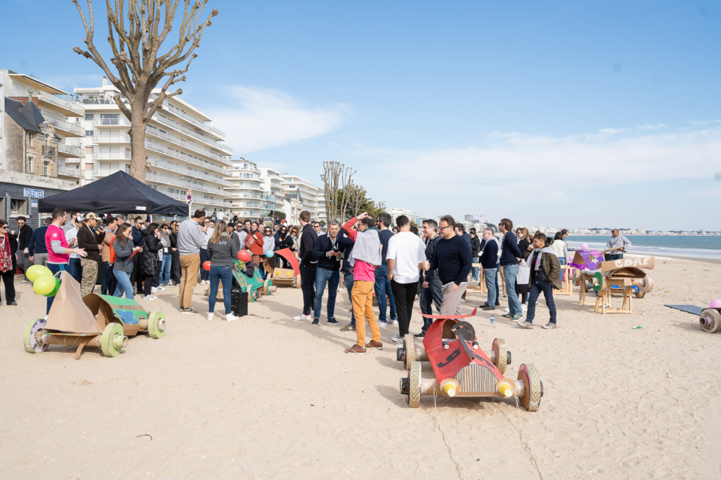 Participants réunis sur une plage autour de caisses à savon fabriquées en équipe avant une course lors d'un challenge de team building.
