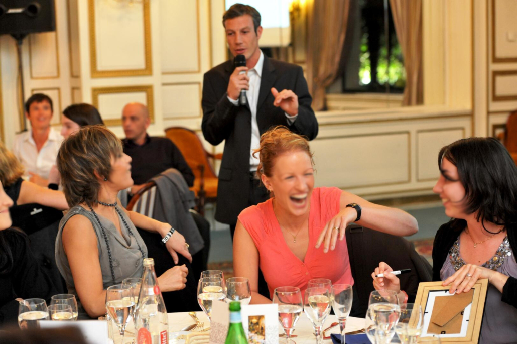 Participants riant et échangeant lors d'une animation de table animée par un maître de cérémonie pendant une soirée événementielle d'entreprise.